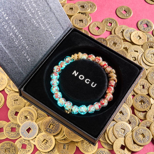 Golden Snake Firefly Glass Swirl Bracelet featuring glowing red and gold beads and 18k gold-plated snake charm in black box surrounded by gold coins by NOGU